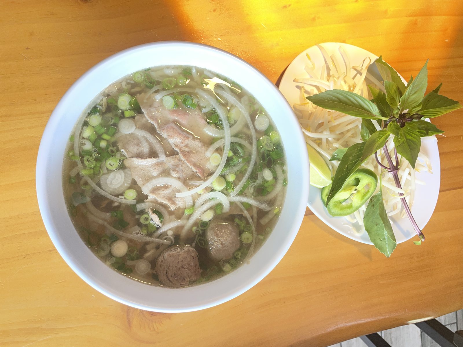 Beef phở with meatballs and a plate of herbs
